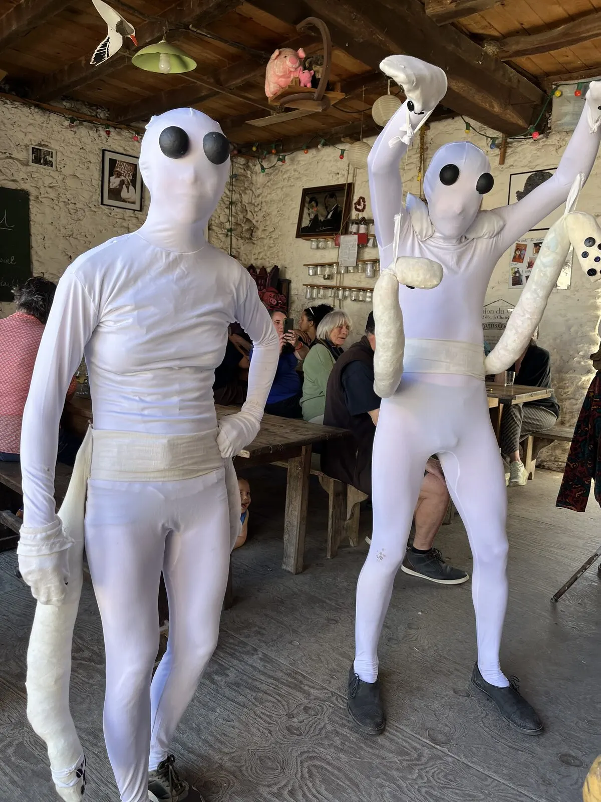 Deux personnes en combinaison blanche et masque d’alien, dans la salle du Café