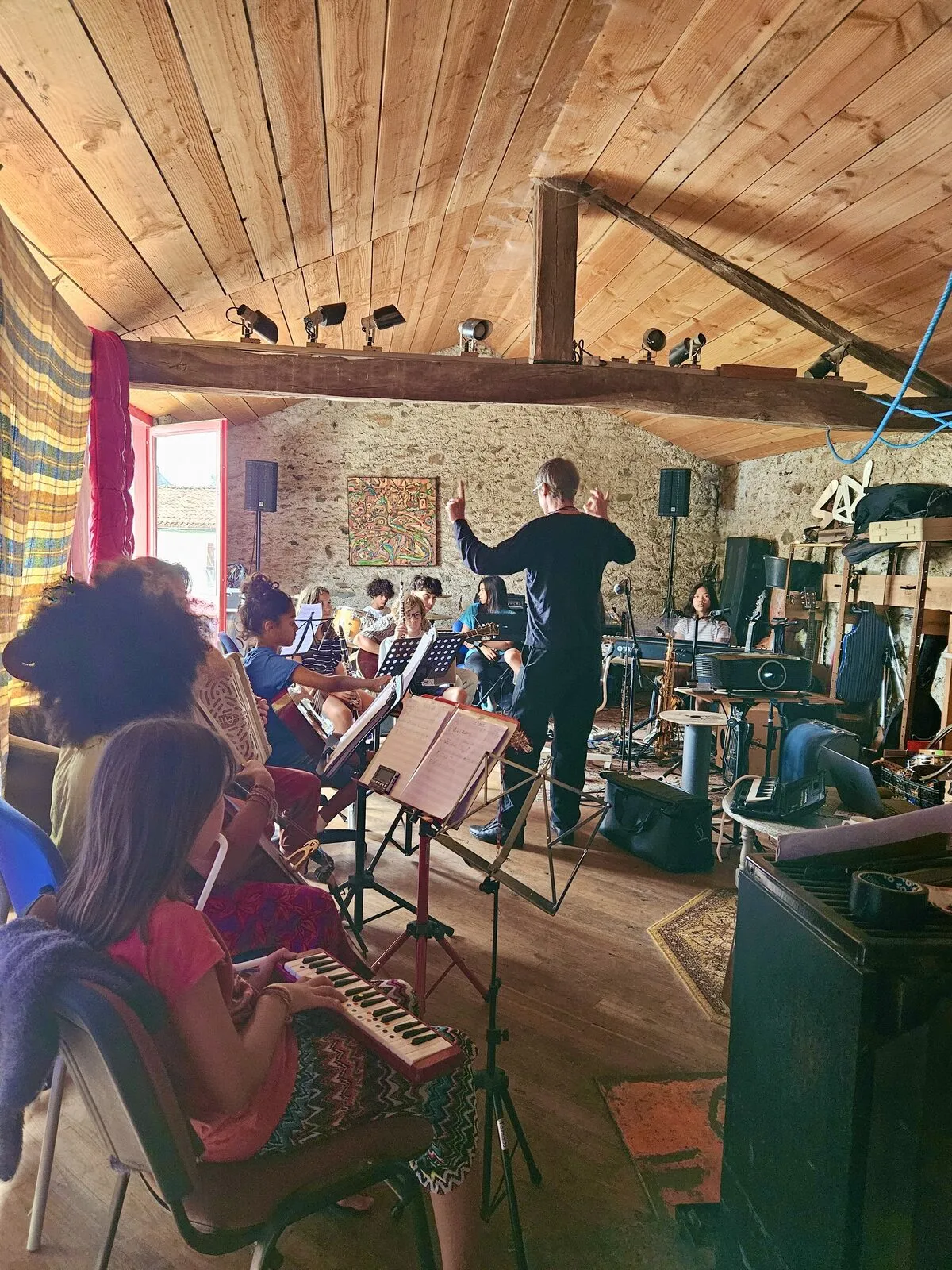 Une dizaine de jeunes musicien·nes et un chef, dans la salle de musique sous charpente
